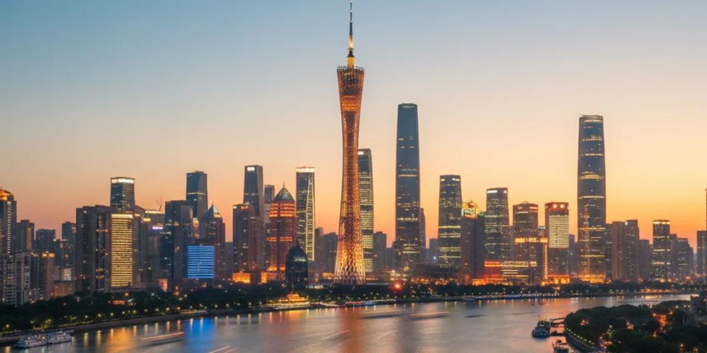 Der Canton Tower leuchtet nachts in bunten Farben über dem Perlfluss, dahinter die Skyline von Zhujiang New Town
