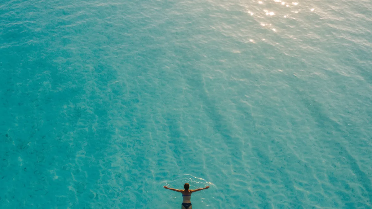 Schwimmerin, die auf dem Rücken im klaren türkisfarbenen Flachwasser treibt, von oben fotografiert